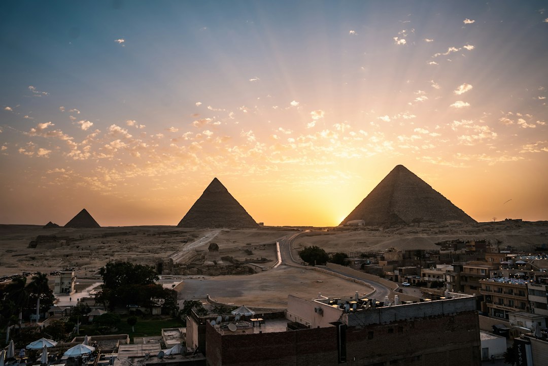 Panoramic sunset view over the three Giza Pyramids with the Sphinx and Cairo city buildings in the foreground