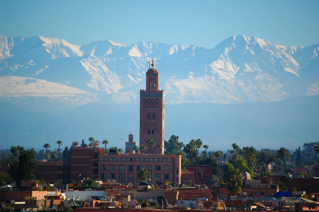 Koutoubia Mosque minaret rising above Marrakech rooftops with snow-capped Atlas Mountains in the background
