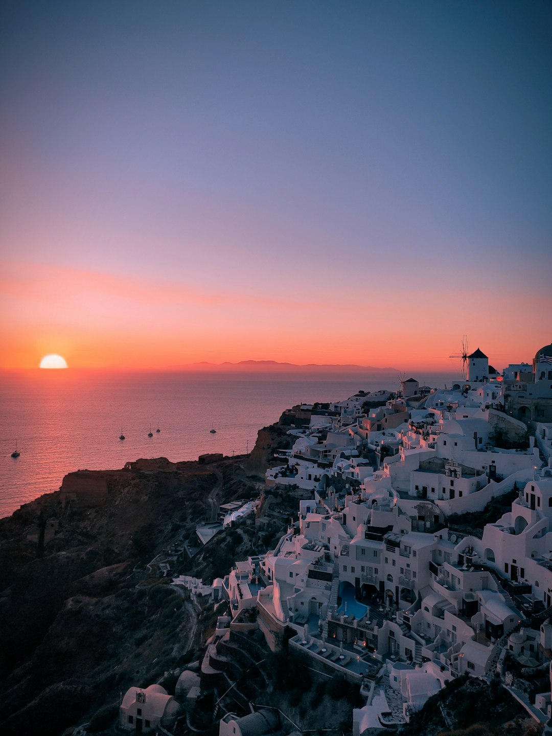 Santorini's Oia village with white-washed cliffside buildings and a windmill at sunset over the Aegean Sea