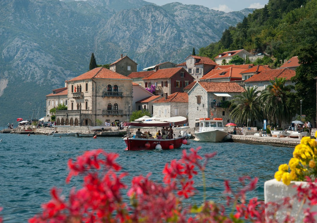 Red-roofed stone buildings along Perast waterfront in Montenegro with boats on the bay and mountains behind