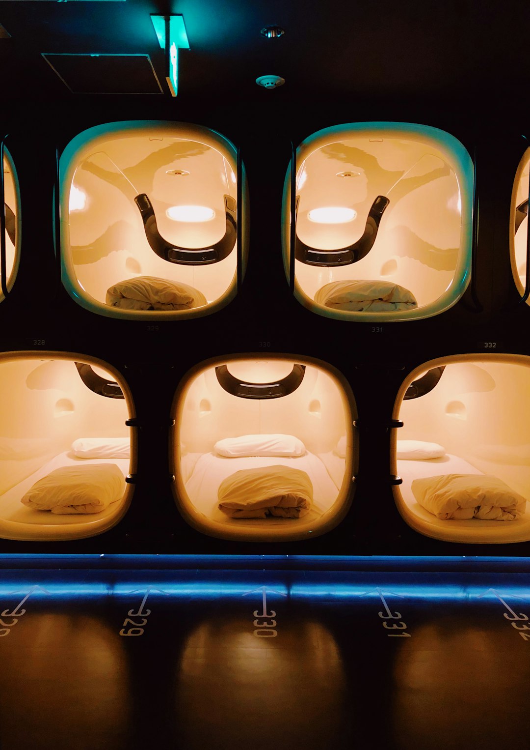 Rows of glowing numbered sleeping capsules with white bedding in a modern Japanese capsule hotel