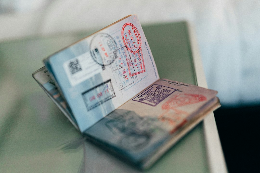 Open passport with multiple colorful entry and exit stamps from various countries, resting on a glass surface