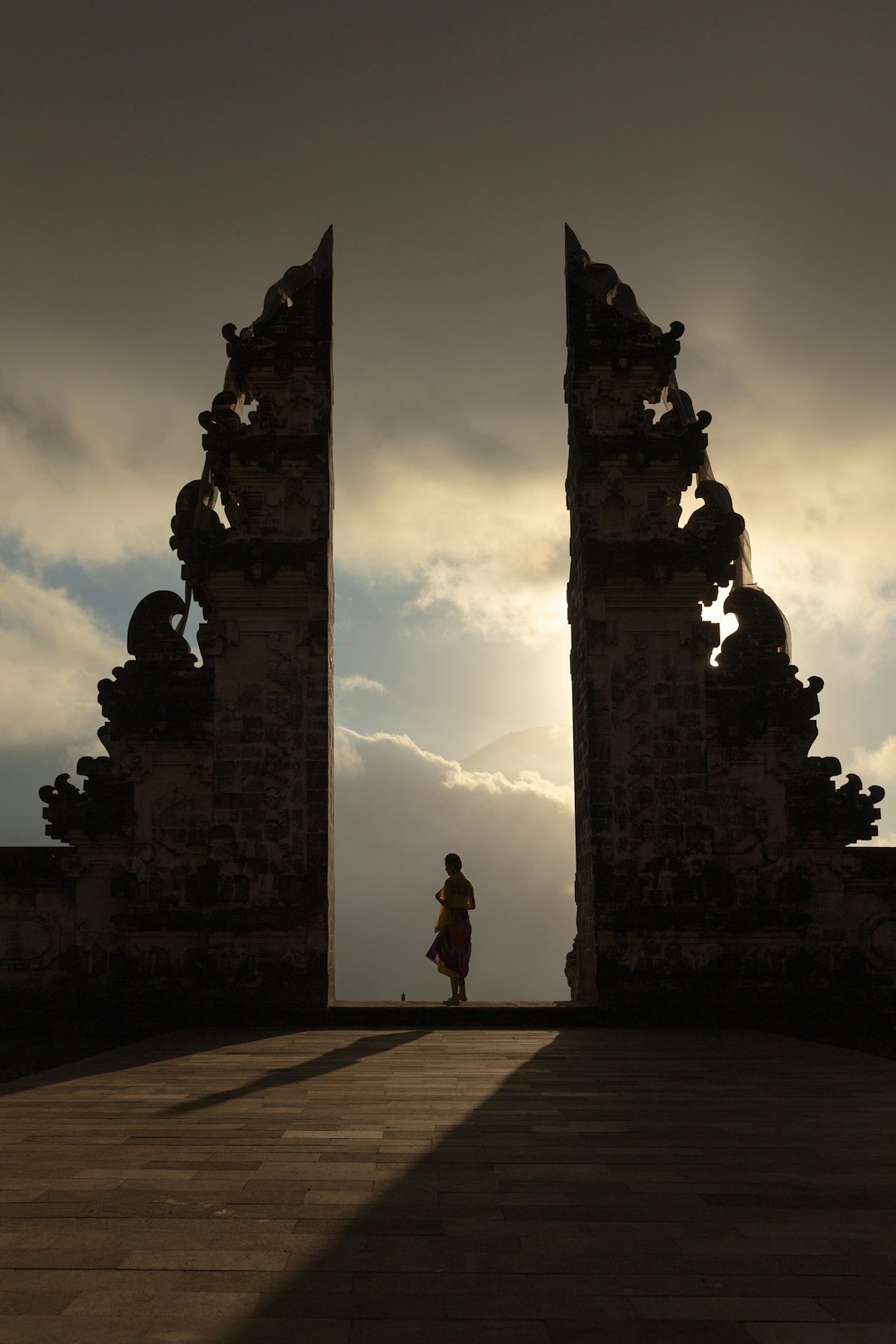 Silhouette of a person standing in the split gate of Lempuyang Temple, Bali, framed by dramatic cloudy sky