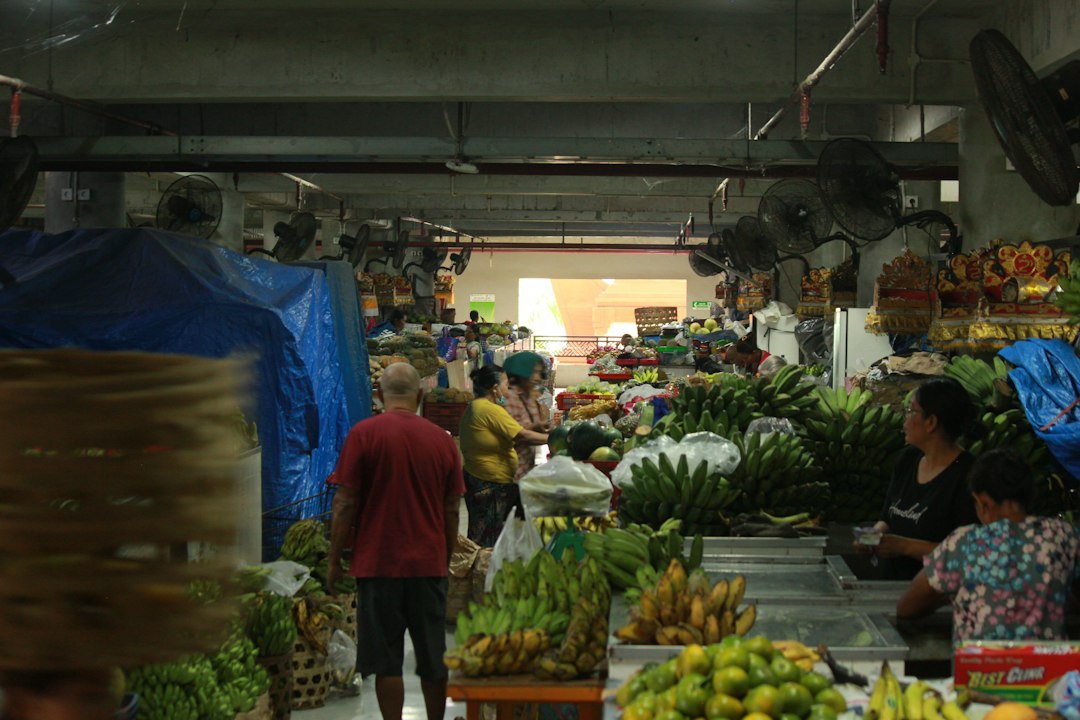 Busy indoor fruit market in Bali with vendors and shoppers surrounded by large bunches of green bananas and tropical fruits