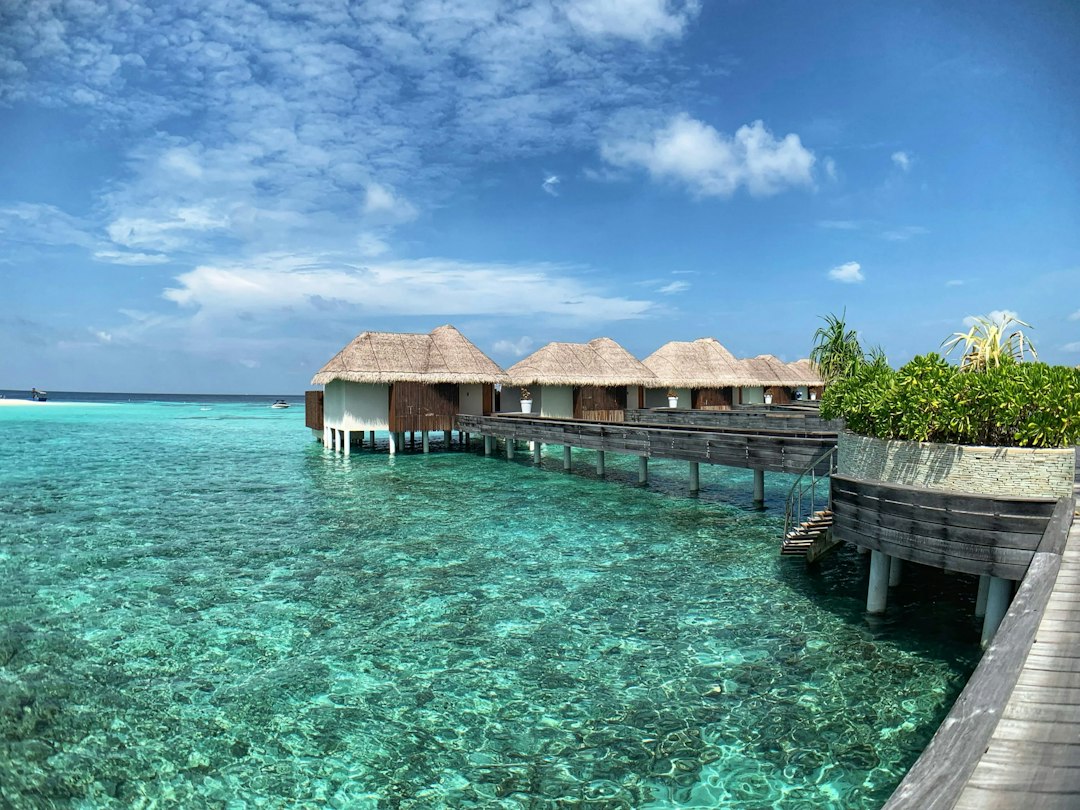 Overwater bungalows with thatched roofs on turquoise lagoon connected by wooden walkway, Maldives resort