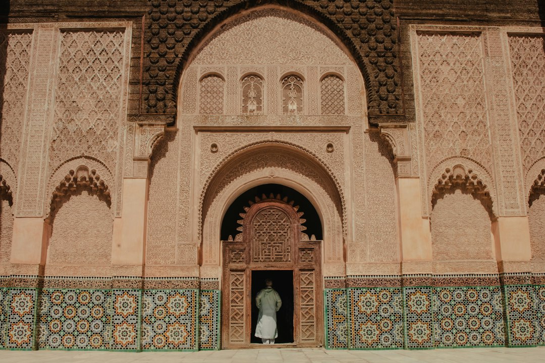 Person entering ornate arched doorway of Ben Youssef Madrasa in Marrakech, with carved stucco walls and zellige tilework