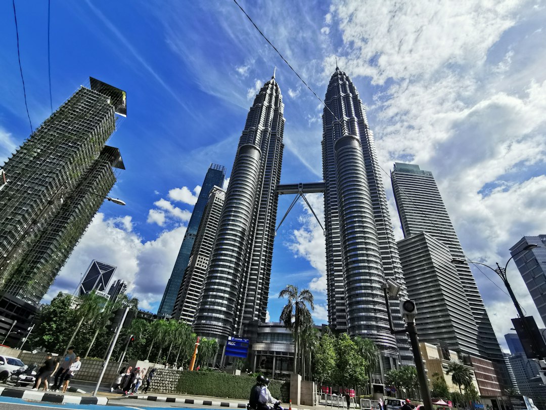 Petronas Twin Towers soaring above Kuala Lumpur skyline on a sunny day with palm trees and pedestrians below