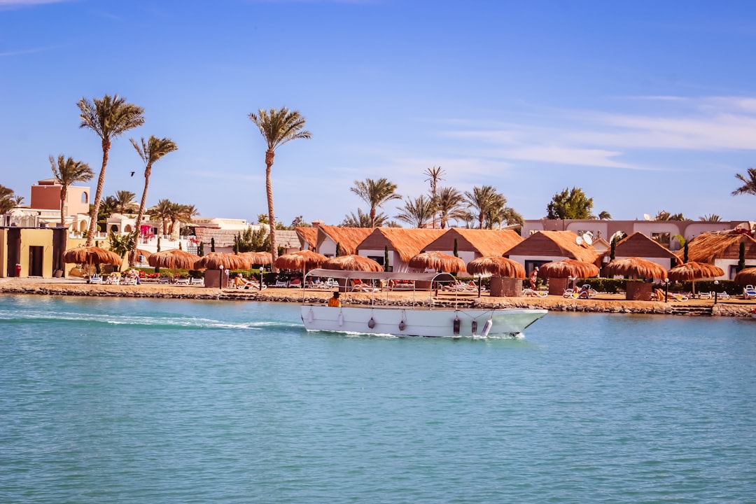 White boat cruising turquoise waters past thatched beach umbrellas and palm-lined resort shore in Hurghada, Egypt